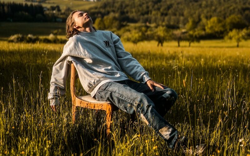 man in gray hoodie sitting on brown wooden chair on green grass field during daytime