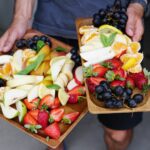 a person holding two trays of fruit