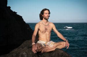 topless man in brown shorts sitting on rock near sea during daytime