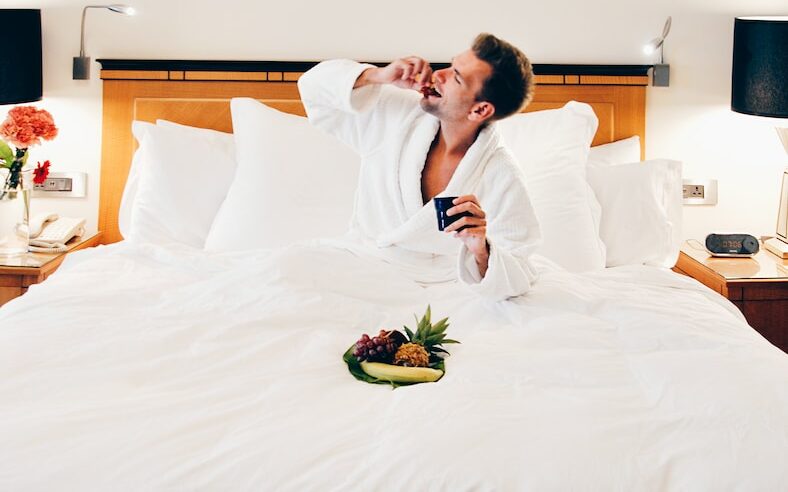 man wearing bathrobe eating on bed