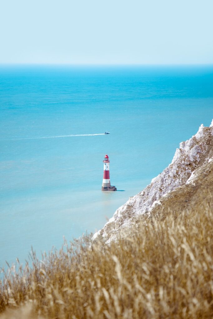 white and red lighthouse on cliff near body of water during daytime
