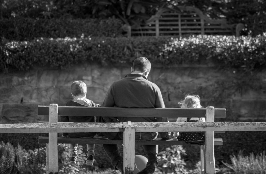 grayscale photography of man and two children sitting in bench